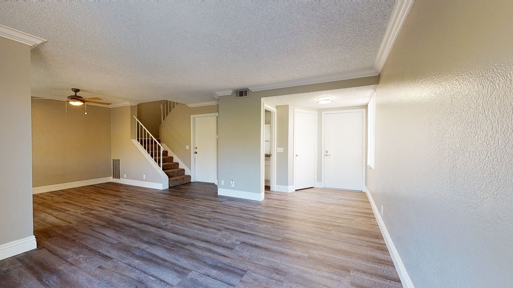 Apartments in Ontario CA - Rancho Vista - Unfurnished Living Room With Wood Styled Flooring, a View of the Dining Room, and Adjacent Entryway and Guest Bathroom at Rancho Vista Townhomes, Ontario, CA