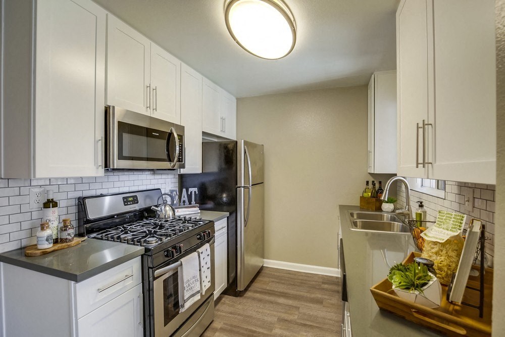 Apartments for Rent in Temecula - Vista Promenade Kitchen with White Cabinetry, Stainless Appliances, Quartz Countertops, Harwood Flooring, and Beige Walls at Vista Promenade Apartments, Temecula, CA