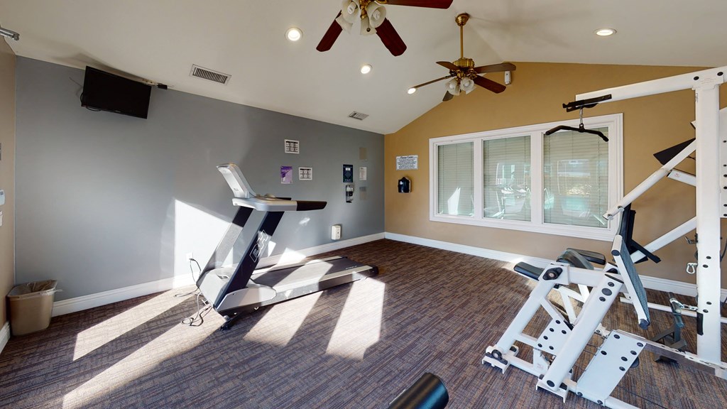 Apartments for Rent Ontario CA - Rancho Vista - Resident Gym With Various Exercise Machines, Several Sets of Windows, and a View of the Pool at Rancho Vista Townhomes, Ontario, CA