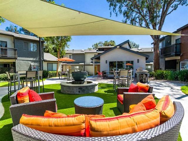 Shaded Outdoor Lounge With Comfortable Seating, Modern Decor, Shade Coverings, Grass, Trees, And Walkways at Encore Apartments, Ontario