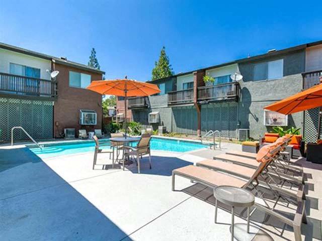 Apartments for Rent Ontario - Encore - Pool Area with Lounge Chairs, Side Tables, and Orange Umbrellas at Encore Apartments, Ontario, CA, 91764