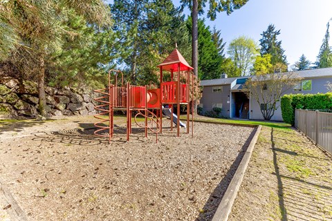 A playground with a red swing set in the middle of a gravel area.