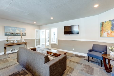 A living room with a grey couch and a painting on the wall.