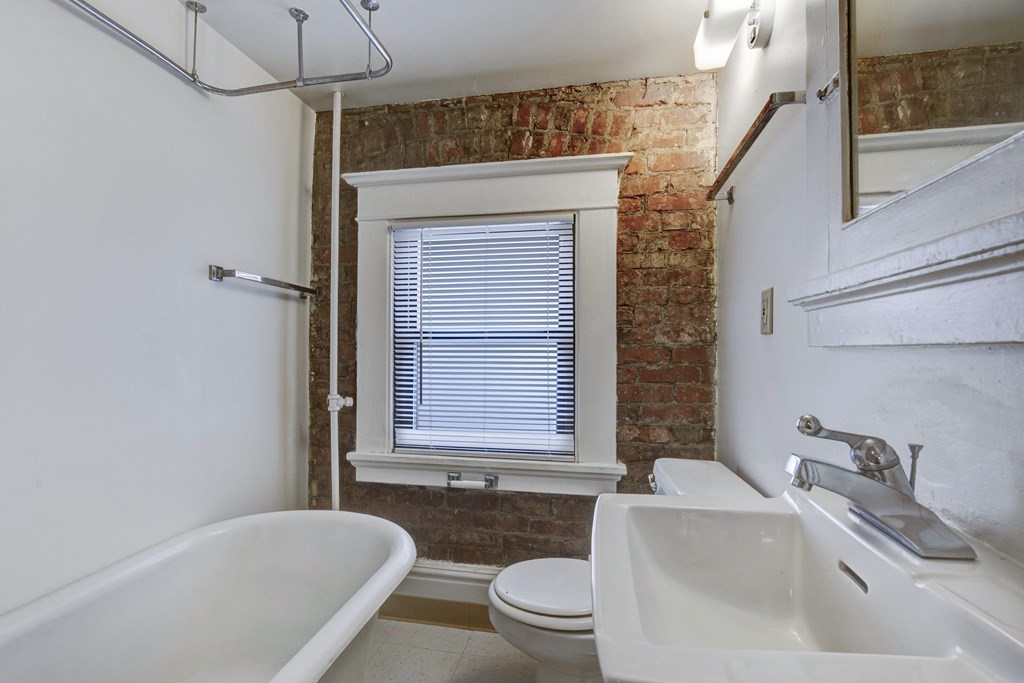 A white bathroom with a brick wall and a window.