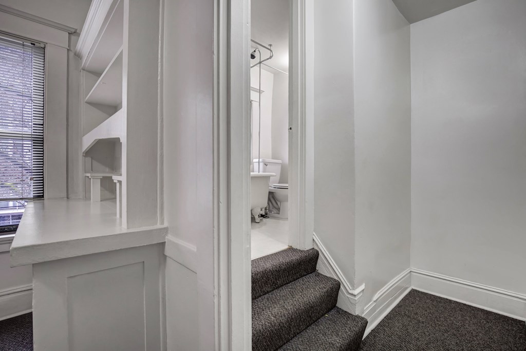 A staircase with a carpeted runner and a white wall.