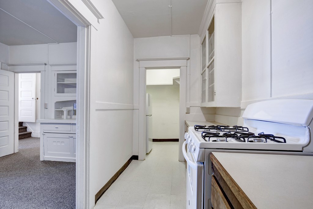 A white kitchen with a stove and a doorway leading to another room.