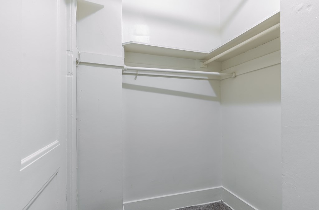 A white closet with a shelf and a white door.