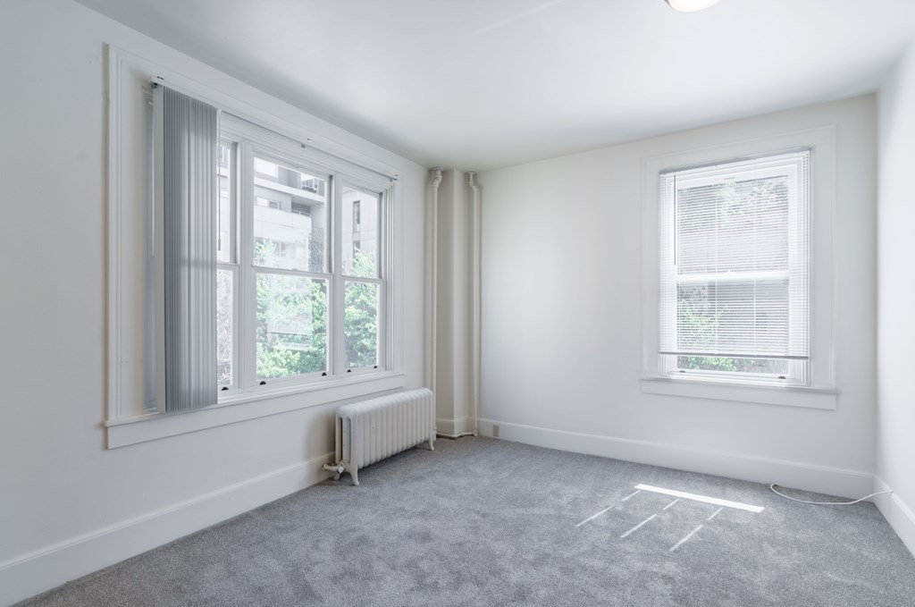 A room with two windows and a radiator on the floor.