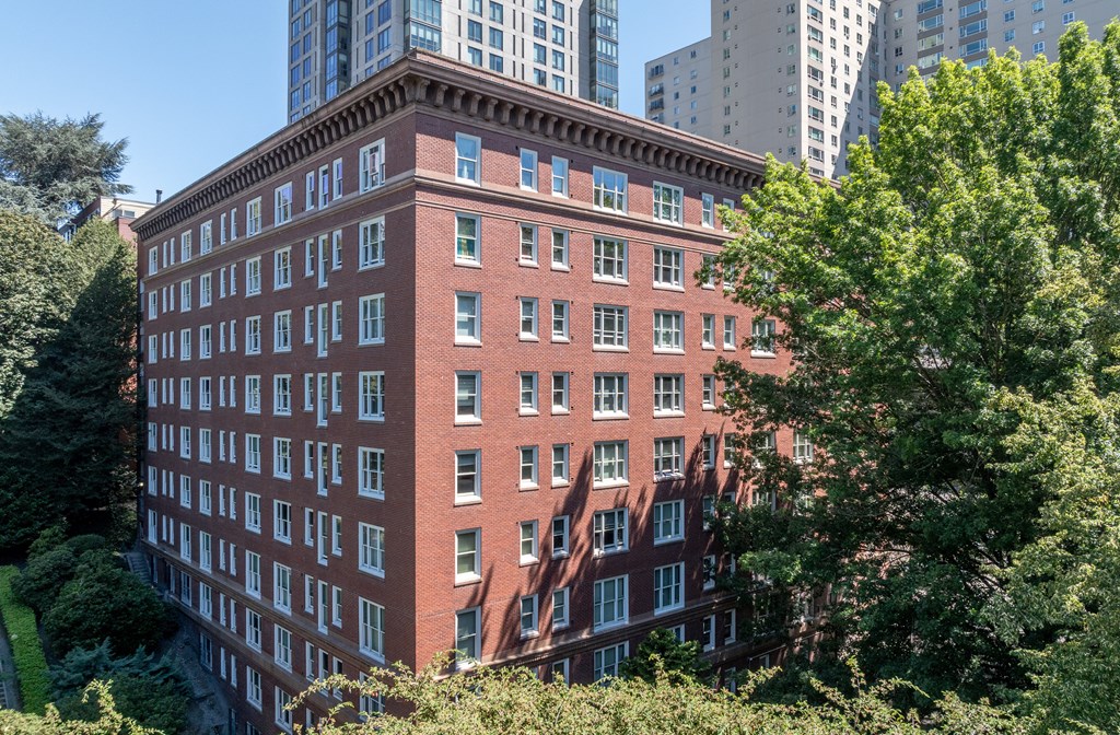 A red brick building with many windows is surrounded by trees.