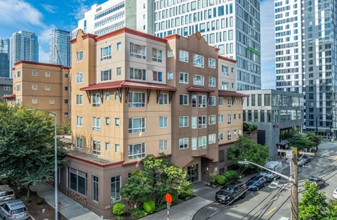 A brown building with a red roof is in the foreground with cars parked in front.