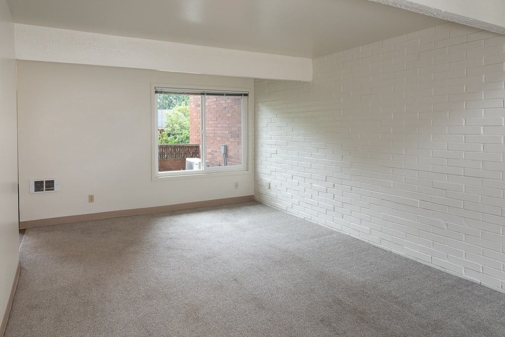 an empty living room with a brick wall and a window