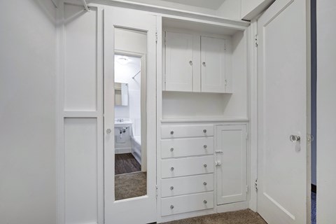 A white cabinet with drawers is open to a bedroom.