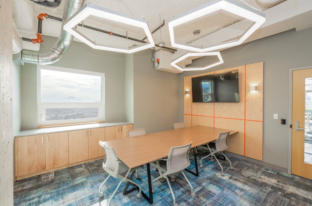 A conference room with a long table and chairs, a television on the wall, and a window with a view of the sky.