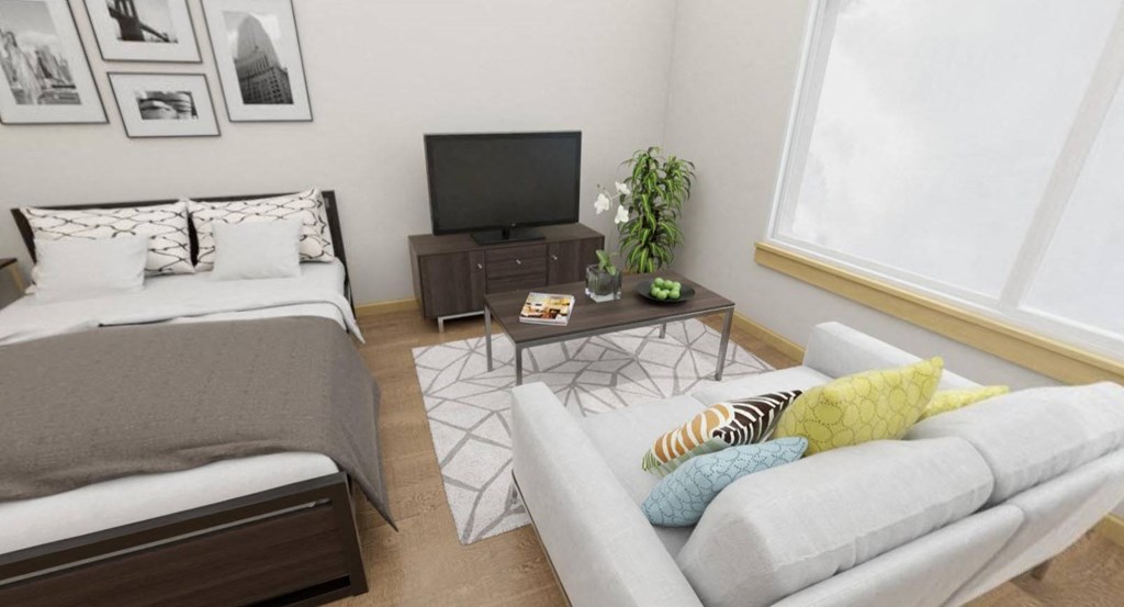 A living room with a grey couch, a bed, a coffee table, and a television.