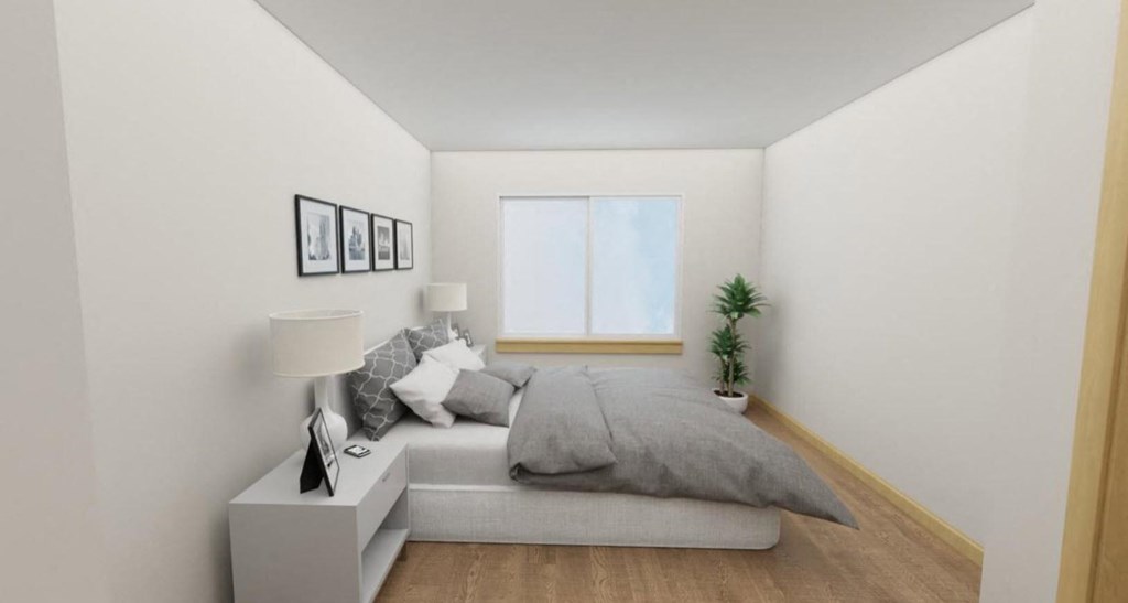 A small bedroom with a bed, nightstand, and a plant.