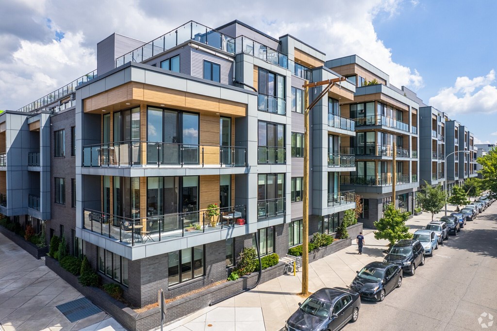 A row of modern apartment buildings with cars parked in front.