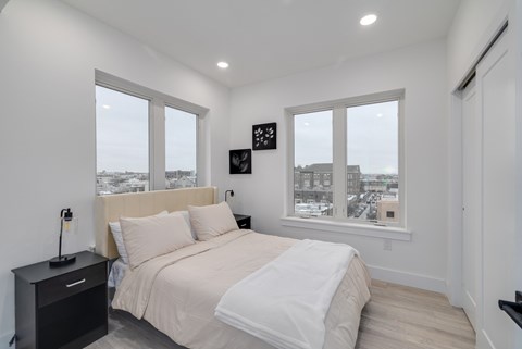 A bedroom with a large bed and a city view through the windows.