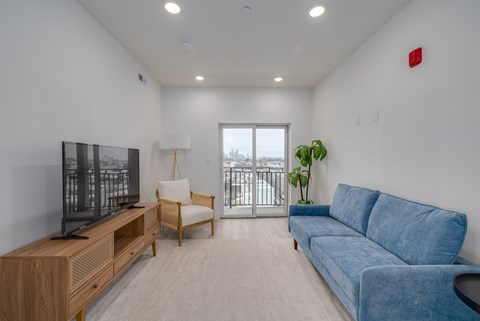 A living room with a blue couch, a wooden entertainment center, and a window with a view of a balcony.