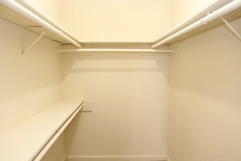 a walk in closet with white walls and a white shelf