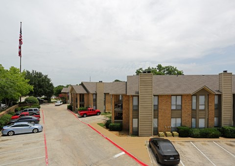 A parking lot with a red car and a black car in front of a building with a flag on top.