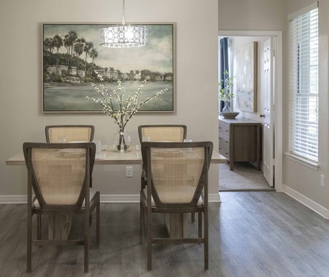 A dining room with a large painting on the wall and a vase with white flowers on the table.