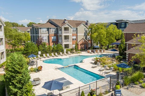 A large swimming pool surrounded by lounge chairs and umbrellas in a residential area.
