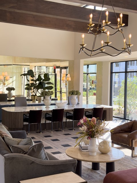 A modern living room with a large grey sofa, a round table with a vase of flowers on it, and a chandelier hanging from the ceiling.