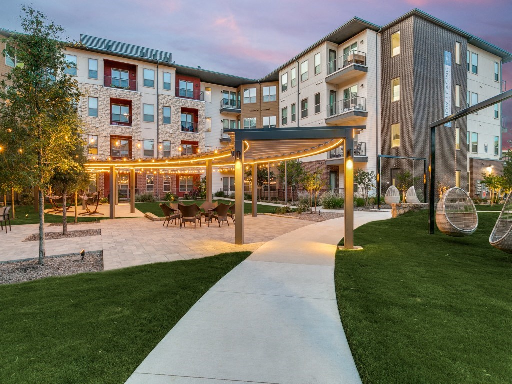 an exterior view of an apartment complex with a patio and lawn