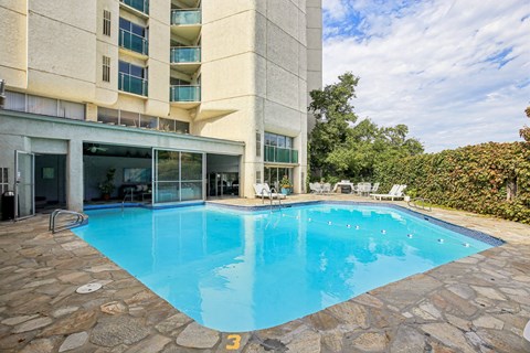 A swimming pool in front of a building with a stone border.