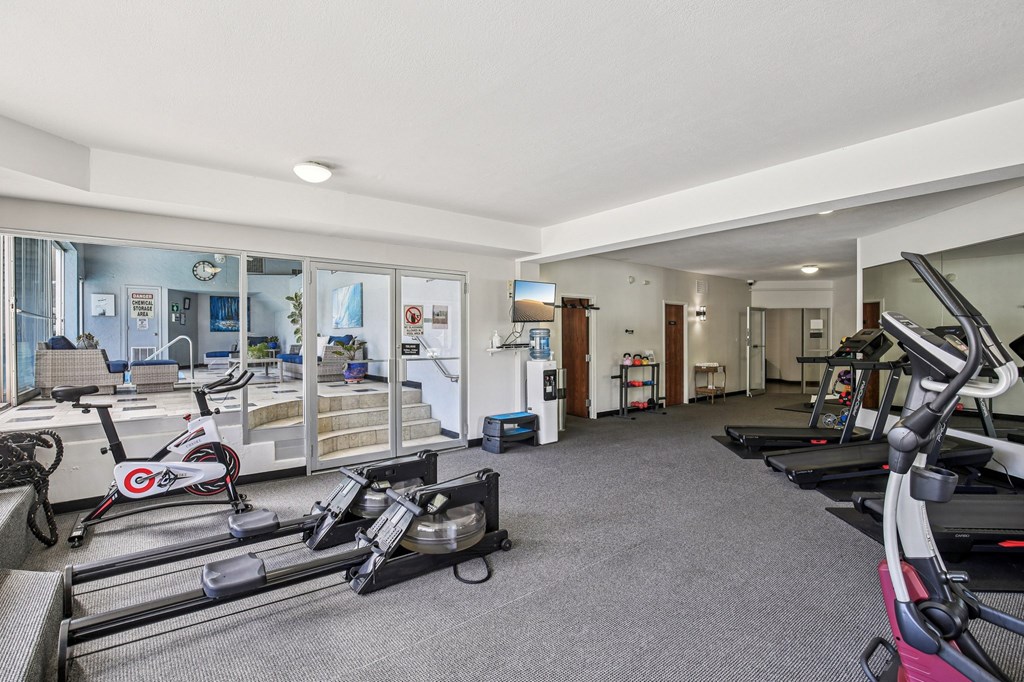 A gym with a variety of equipment including treadmills, stationary bikes, and weights.