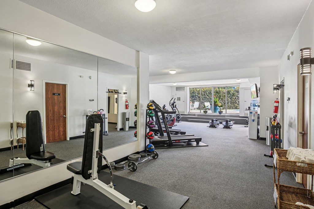 A gym with a variety of equipment including a bench press, a treadmill, and a rowing machine.