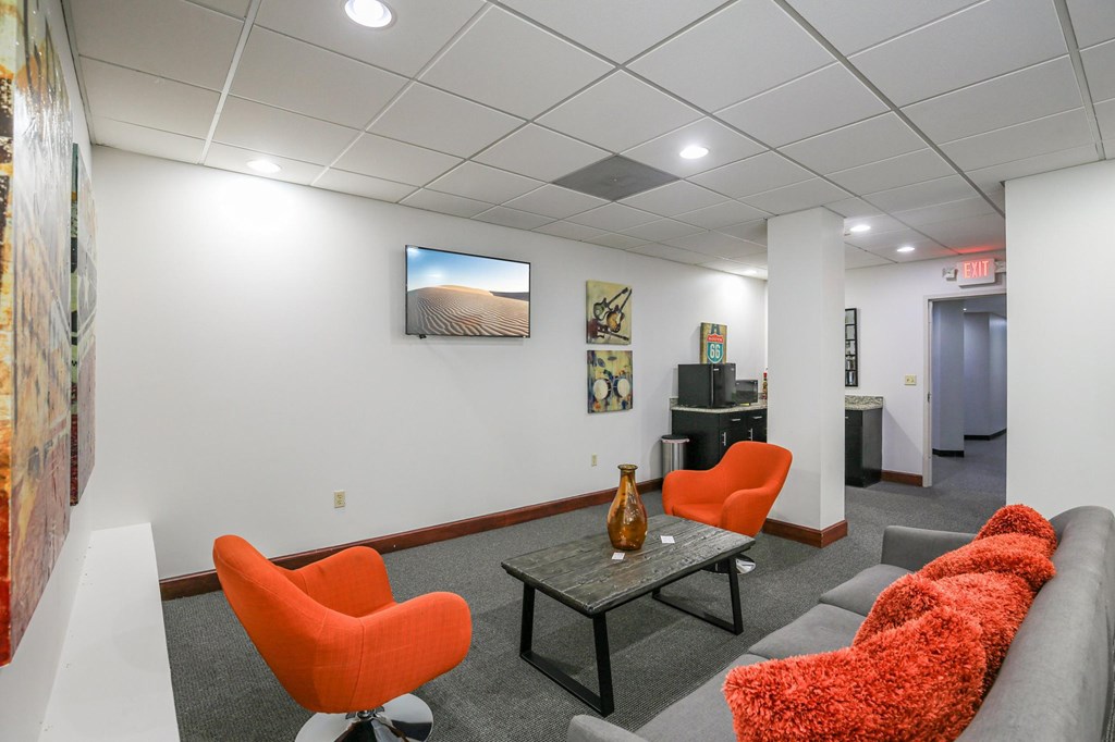 A living room with a grey couch, orange chairs and a painting on the wall.