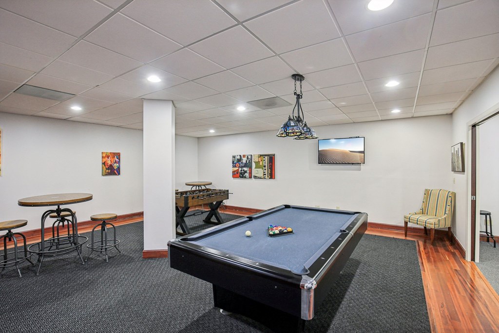 A pool table is in the middle of a room with a TV mounted on the wall.