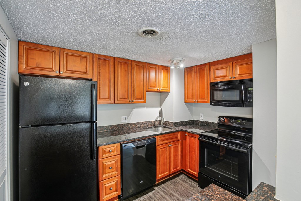 A black refrigerator is in a kitchen with wooden cabinets.