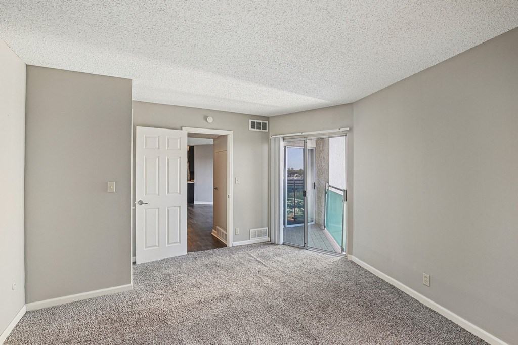 A room with a carpeted floor and a sliding glass door leading to a balcony.