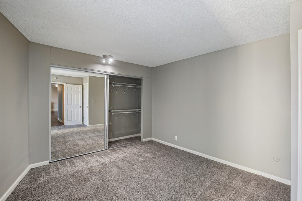 A spacious room with a carpeted floor and a closet with a mirror.