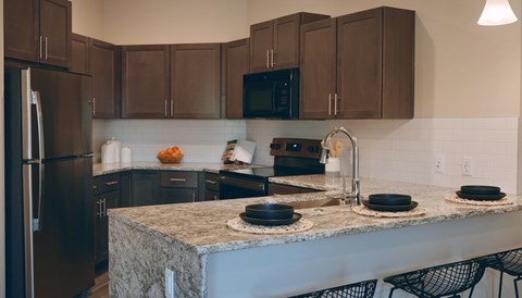 A kitchen with a granite countertop and black chairs.