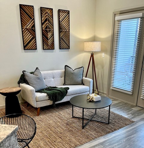 A living room with a grey couch, a black metal chair, and a table with a lamp on it.