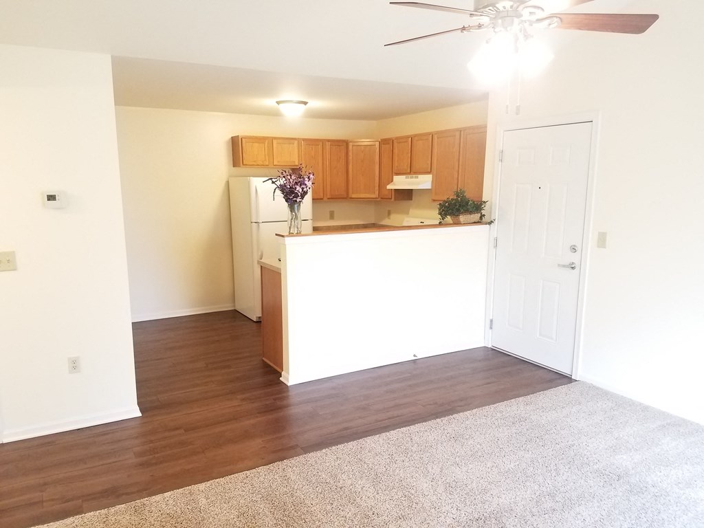 an empty living room with a kitchen and a ceiling fan