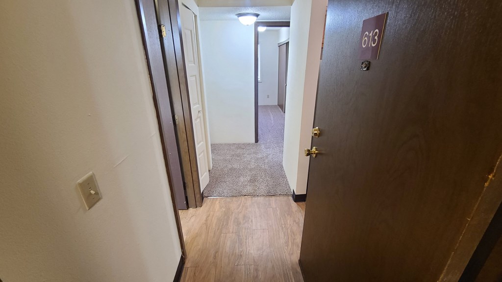 a door is open to a hallway with a carpeted floor and an open door