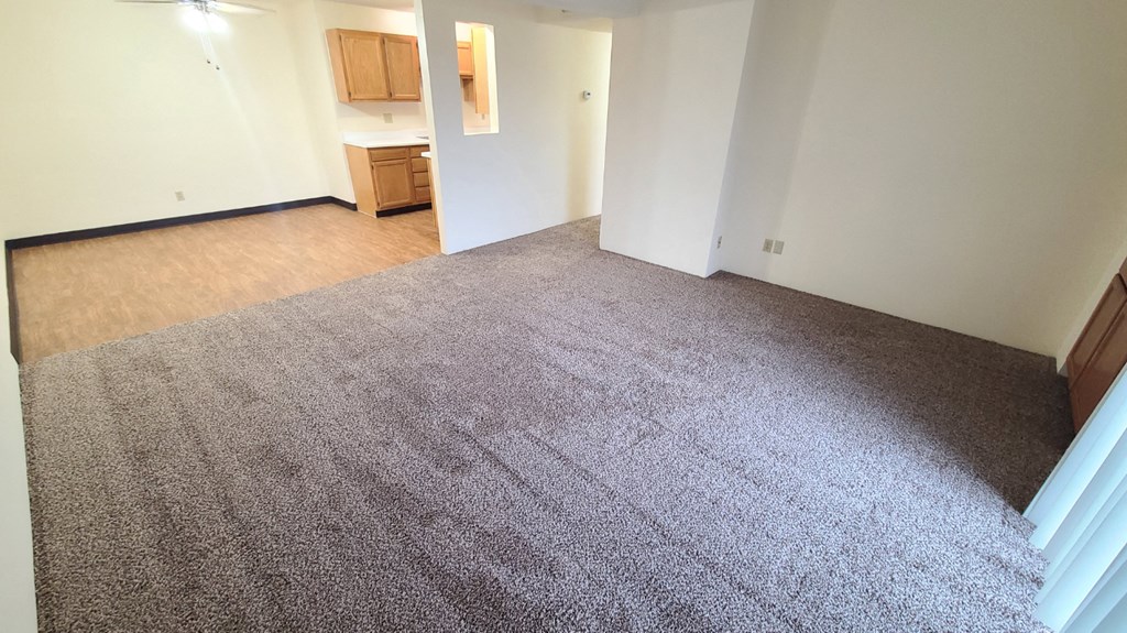an empty living room with carpet and a kitchen