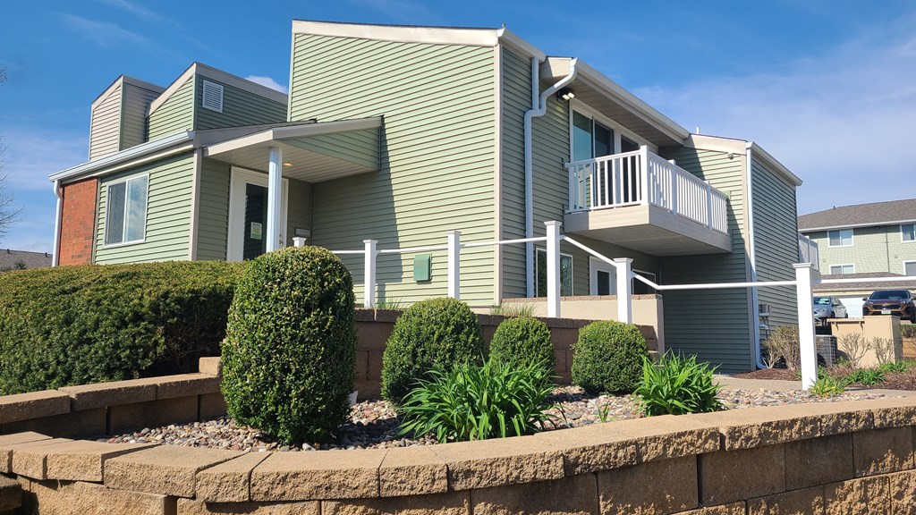 a green house with a balcony and a retaining wall