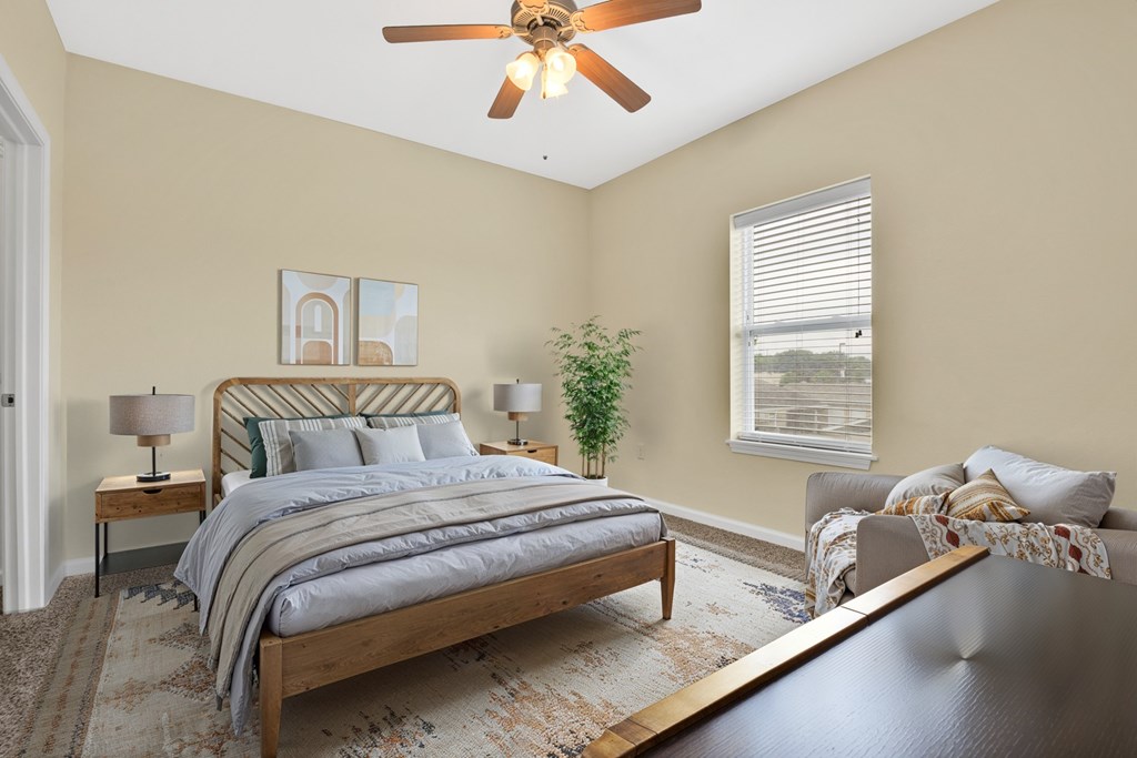 A bedroom with a bed, a couch, a ceiling fan, and a window.