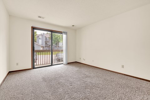A room with a carpeted floor and a sliding glass door leading to a balcony.