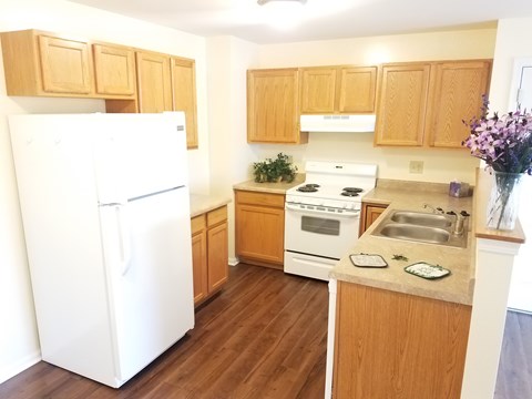 A white refrigerator stands in a kitchen with wooden cabinets and a stove.