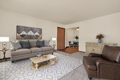 A living room with a grey couch, a coffee table, a brown leather chair, and a painting on the wall.