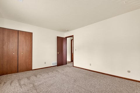 A room with a carpeted floor, a brown door, and a brown wardrobe.
