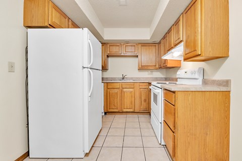A white refrigerator stands in a kitchen with wooden cabinets and a white stove.