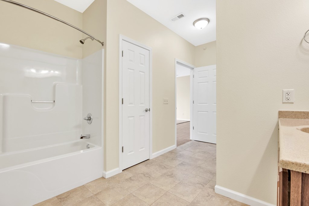 A bathroom with a white tub and shower, a sink, and two doors.