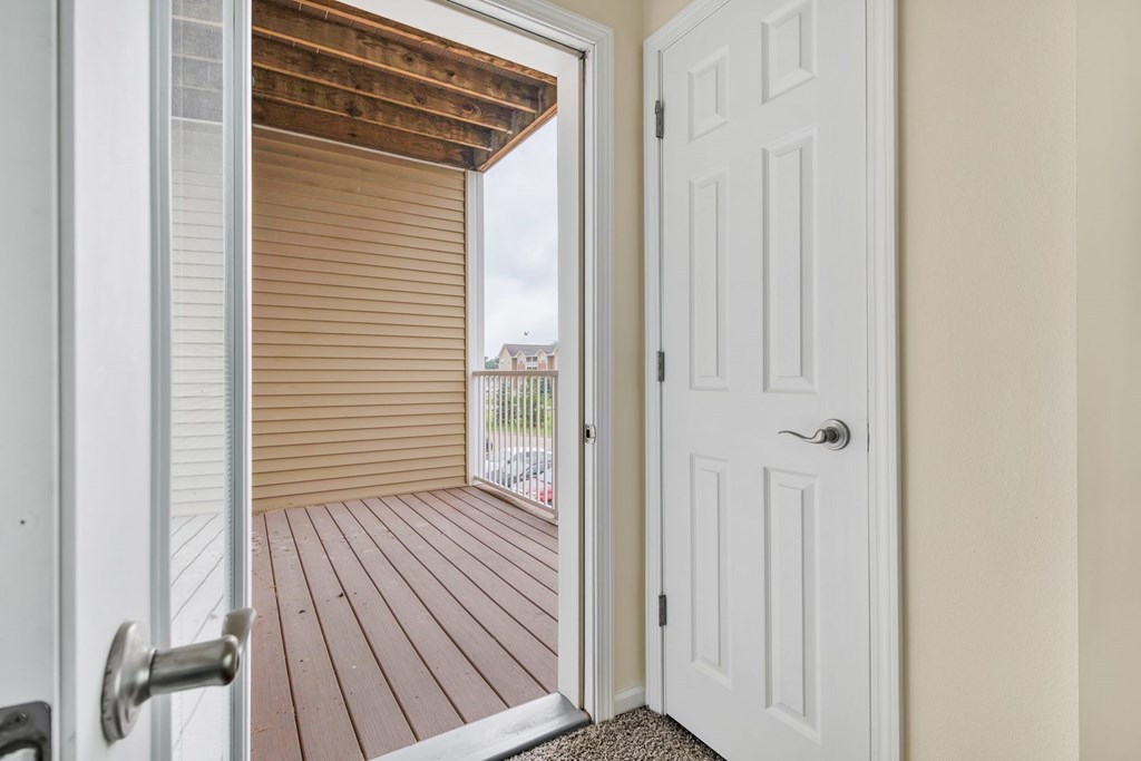 A white door is open to a deck with a sliding glass door.